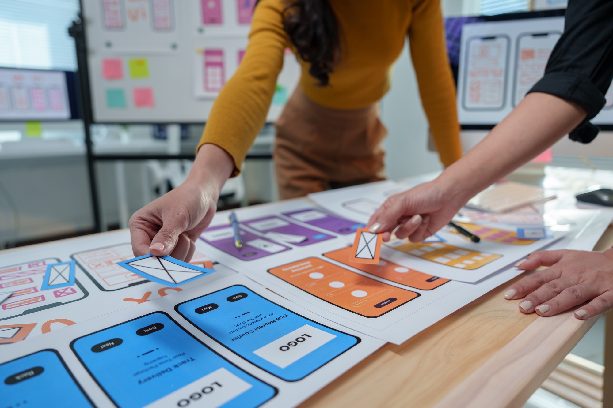 Two skilled web designers are working together, placing icons on a large paper mockup of a mobile ap